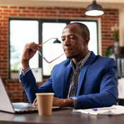 A man in a blue suit and tie sitting at a table with a laptop.