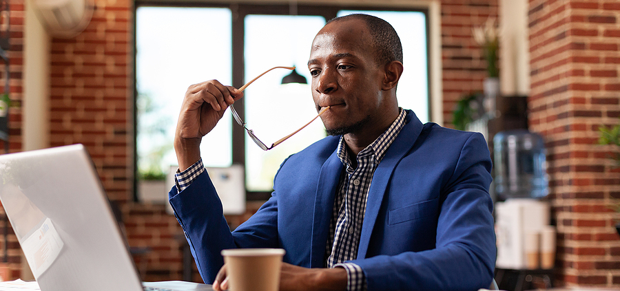 A man in a blue suit and tie sitting at a table with a laptop.