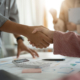 Two people shaking hands over a table.