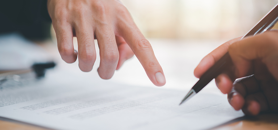 Two people are signing a document with one hand and the other holding a pen.