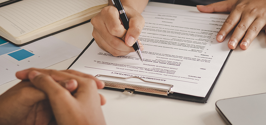 A person writing on paper with another person holding a pen.