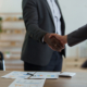 Two men shaking hands over a table with papers.